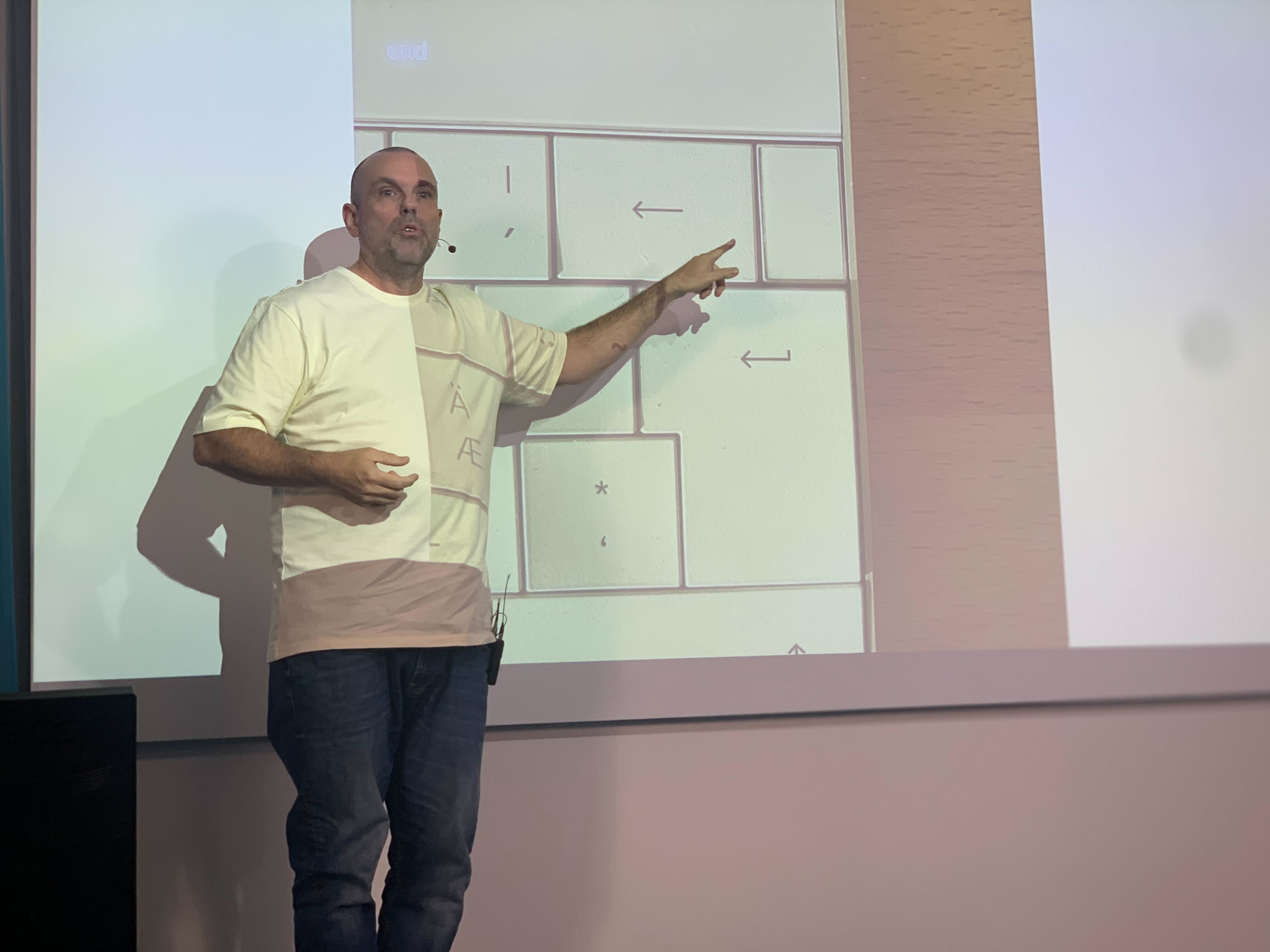 En man står på en scen och pekar på en presentation som projiceras bakom honom.