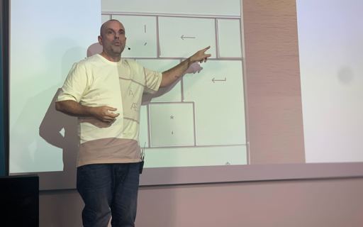 Tillgängliga gränssnitt för e-handel En man står på en scen och pekar på en presentation som projiceras bakom honom.