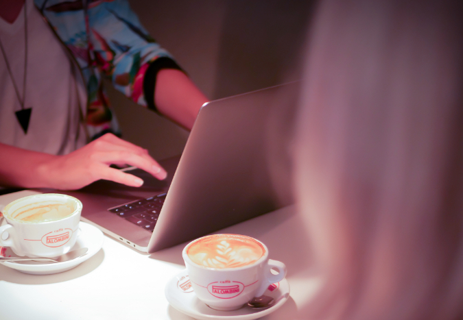 Ett bord med två kaffekoppar och en uppslagen laptop. Två personer skymtar i utkanten av bilden.