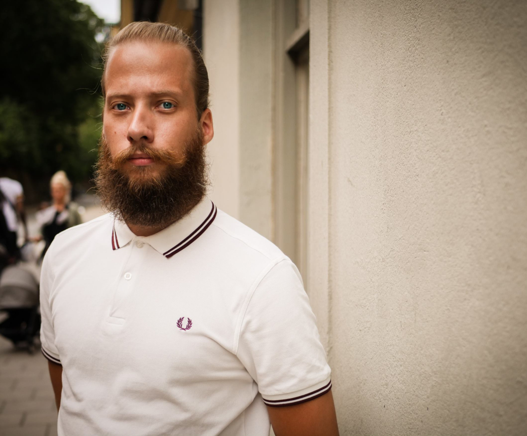 Fred står framför en vit husfasad. Han ser allvarlig ut, har skägg och en vit tröja.