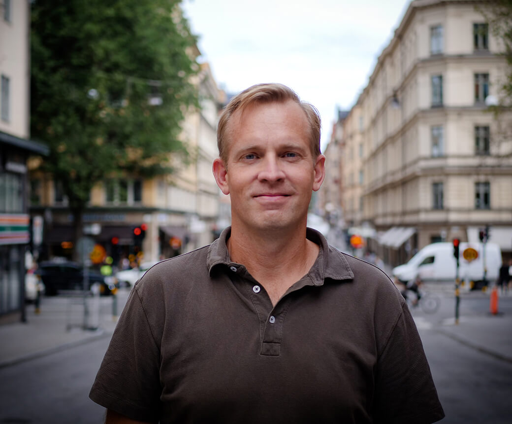 Markus står i en livlig stadsmiljö. Han har blont kort hår och en grön tröja.