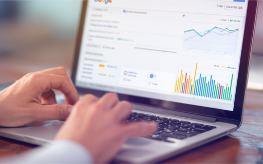 Närbild på händer som skriver på en laptop med Google Analytics öppet, som visar grafer och stapeldiagram med statistik