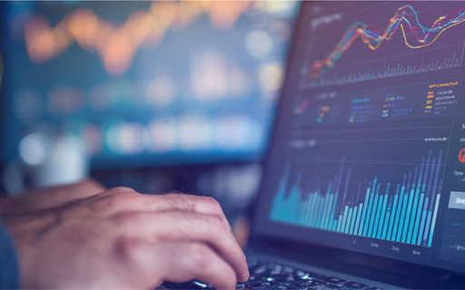 Händer på tangentbord framför en laptopskärm med grafer och dataanalys.